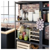 Modern black metal kitchen shelf unit with jars, bottles, and garlic. Brick wall backdrop, wooden countertop with sink.