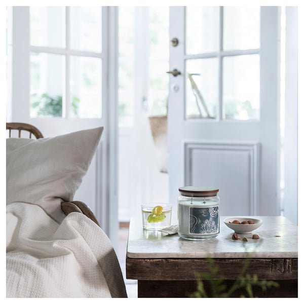 A cozy room with a white door, bed, and table. On the table, a clear glass candle, a glass of water with lemon, and a bowl of nuts.