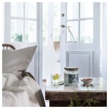 A cozy room with a white door, bed, and table. On the table, a clear glass candle, a glass of water with lemon, and a bowl of nuts.