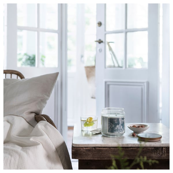 Cozy room with white bed, glass candle, bowl, and lemon drink on table by window.
