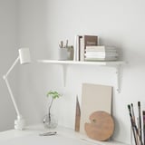 White BURHULT wall shelf with books & art supplies.