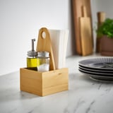 Small wooden box, CHOKLADHAJ, holds jars, spoons, napkins. Marble counter, plates nearby. Stands alone, fits neatly.