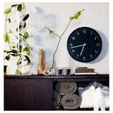 Top shelf: black clock, clear candles, glass vases with plants. Bottom shelf: woven basket, folded blankets. Clear CYLINDER vase with green plant.