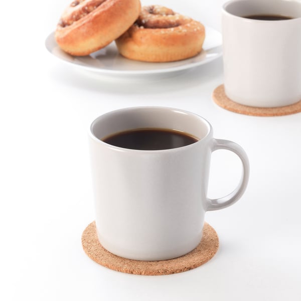 Two mugs, one with coffee, on cork coasters. Two pastries behind. Rustic table setting with DINERA stoneware.