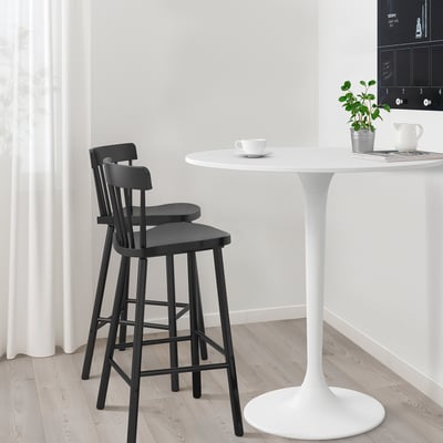 Two black bar stools sit at a white round bar table, with a small white cup on top.
