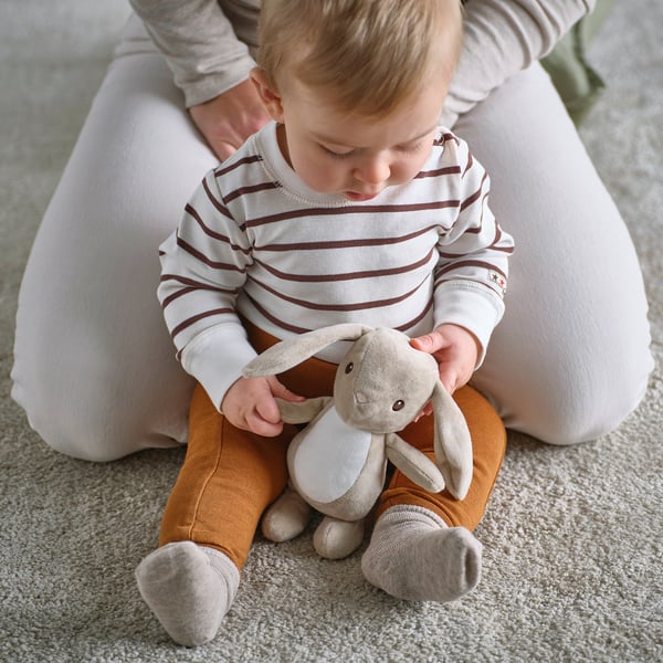 Baby sits, holding stuffed bunny toy, both comfortable and safe for play.