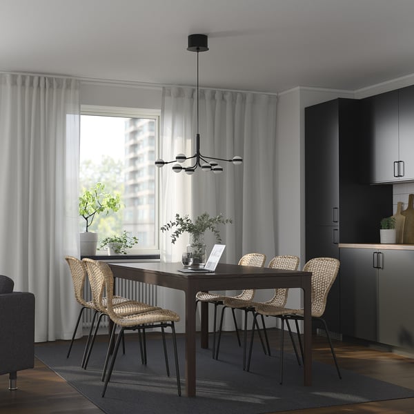 Modern dining setup with wooden EKEDALEN table, chairs, and laptop. Large window with light curtains. Room is spacious and minimalist.
