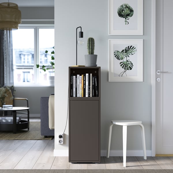 Gray EKET storage unit with door & shelves, between plant art, stool, & cactus.