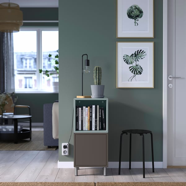 Modern gray storage unit with shelves, drawers, and a cactus, beside a door in a bright room.