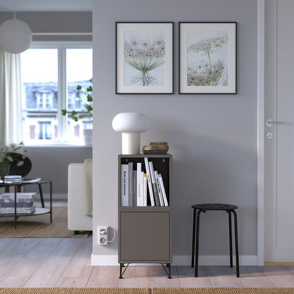 Modern living room with black EKET storage, books, decor, and floral art prints.