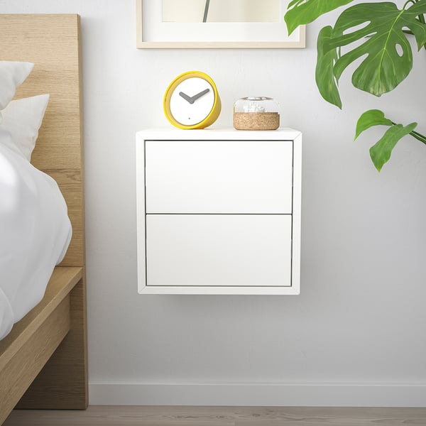 White EKET cabinet with 2 drawers, yellow clock, wooden bed, green plant leaf, minimalist bedroom.