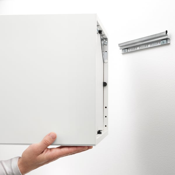 Hand holding wall-mounted white cabinet with visible suspension rail, demonstrating its ease of access and adjustable shelving functionality.