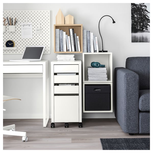 Modern office setup with white EKET storage unit, grey sofa, laptop, wooden decorations, and books.