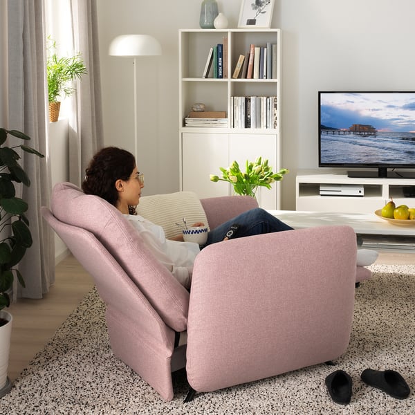 Woman reclining in pink EKOLSUND armchair, watching tv.