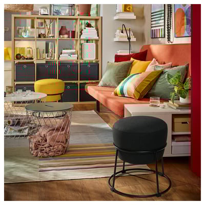 Bright living room with peach sofa, colorful pillows, striped rug, and storage shelves filled with books and decor.
