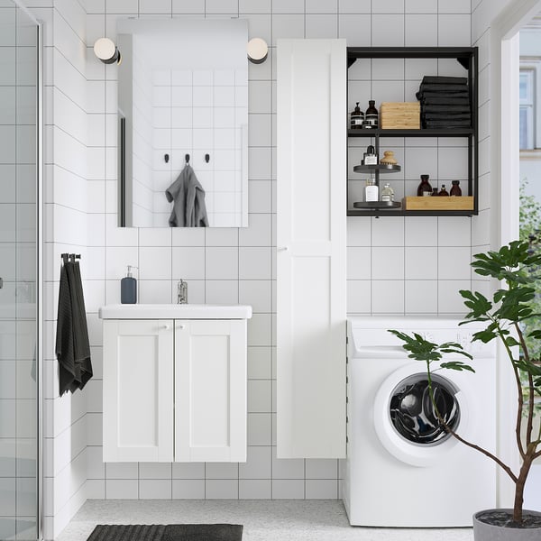 Modern white bathroom with grey accents. Includes vanity, mirror, shower, washing machine, and plant. Mirrored cabinet with towels above sink.