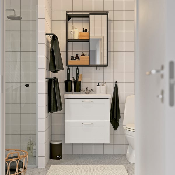 Modern bathroom with white ENHET vanity, mirror, and black accessories. Towels hang on minimalist hooks.