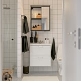 Modern bathroom with white ENHET vanity, mirror, and black accessories. Towels hang on minimalist hooks.