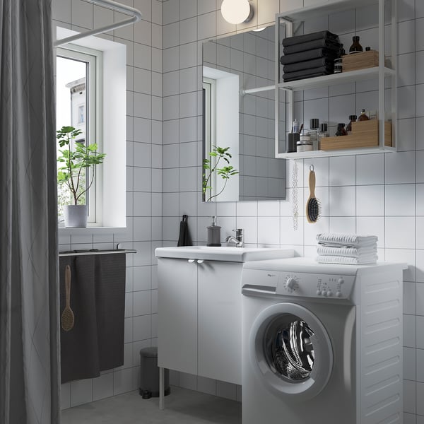 Minimalist bathroom with ENHET storage, front-load washer, mirrored cabinet, shower, and plant.