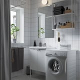 Minimalist bathroom with ENHET storage, front-load washer, mirrored cabinet, shower, and plant.