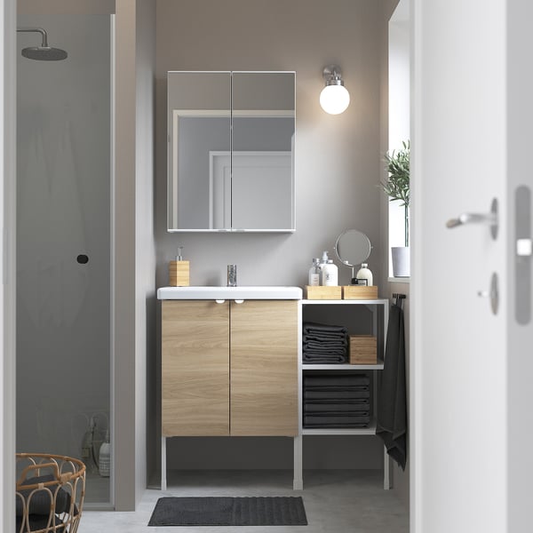 Modern bathroom with light wood ENHET vanity, mirror cabinet, wall light, glass shower, and exit door.