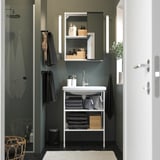 Modern bathroom with white sink, mirror, dark green walls. Towels, items on shelves. Mirror with lights, compact design.