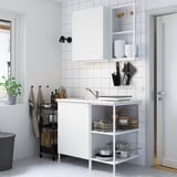 White kitchen with marble counters, stainless sink, and mixed storage. Door leads to another room.