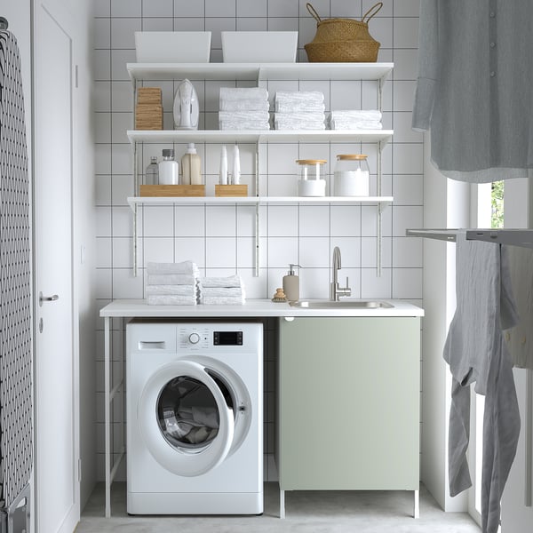 Modern white laundry setup with light green cabinets, washing machine, sink, and organized shelves. Compact yet functional.