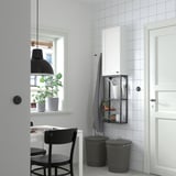Minimalist room with white ENHET cabinet, adjustable black bins, plants, chair, table, and pendant light.