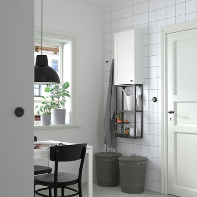 Minimalist room with white ENHET cabinet, adjustable black bins, plants, chair, table, and pendant light.