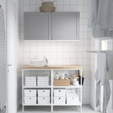Compact laundry room with white tiles, gray cabinet, and organized shelf with towels, cleaning supplies, and an iron.