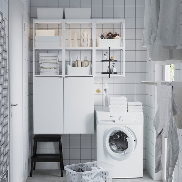 Modern white ENHET laundry unit; large cabinet, open shelves, washing machine, black stool, basket, clean design.