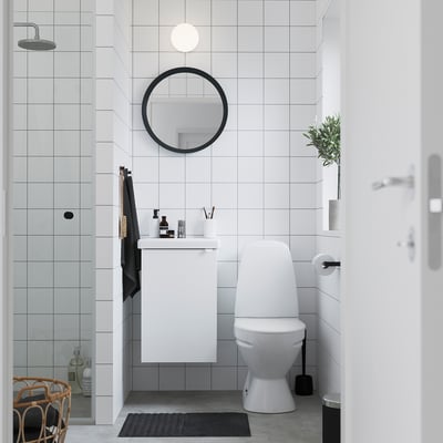 Modern bathroom with ENHET white cabinet, mirror, black accents, grey tiles, and toilet.