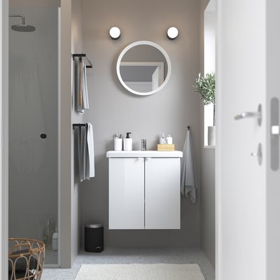 Modern minimalist bathroom: white ENHET cabinet, round mirror, sleek sink, grey towels, silver accents, small plant.