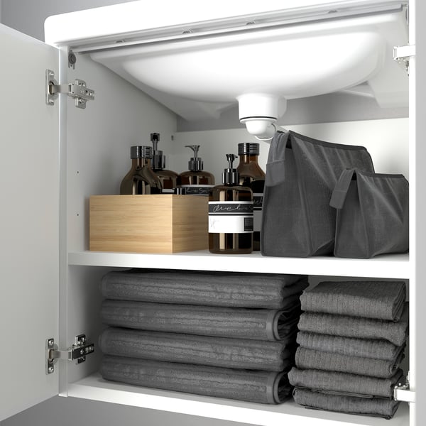 White bathroom cabinet with shelves, storing grey towels and toiletries.