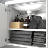 White bathroom cabinet with shelves, storing grey towels and toiletries.