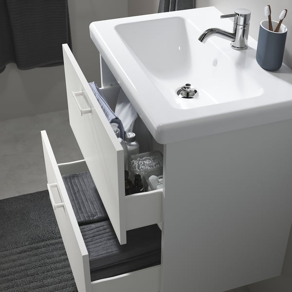 White bathroom vanity with sink, two open drawers revealing toiletries, faucet, and toothbrush holder.