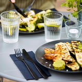 Plate with grilled vegetable slices, accompanied by fork and knife, and a glass cup with garnish.