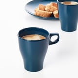 Two blue mugs filled with coffee, set on a white table, accompanied by a plate with biscuits.