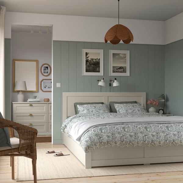 Modern cosy bedroom with white bed, green pillows, storage, art, chair, dresser, slippers.