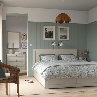 Modern cosy bedroom with white bed, green pillows, storage, art, chair, dresser, slippers.