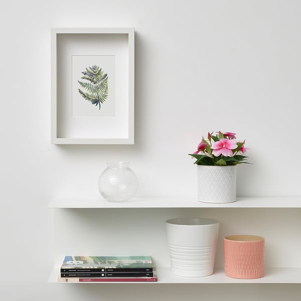 A stylish, white, wall-mounted shelf featuring a framed plant print, a clear vase, a potted artificial plant, and stacked books.