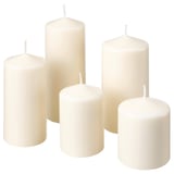 Six white pillar candles of varying heights, made from paraffin and plant-based wax, arranged neatly in a cluster.