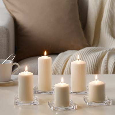 Six white pillar candles in clear glass holders, lit, on a light-colored table, creating a warm and inviting atmosphere.