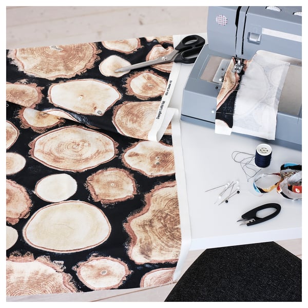 A sewing workspace with FJÄLLTÄTÖRT log-pattern fabric, scissors, and a sewing machine.