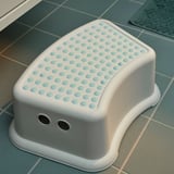 White childs step stool with blue dot texture, rounded edges, and slip-resistant underside on a tiled floor.