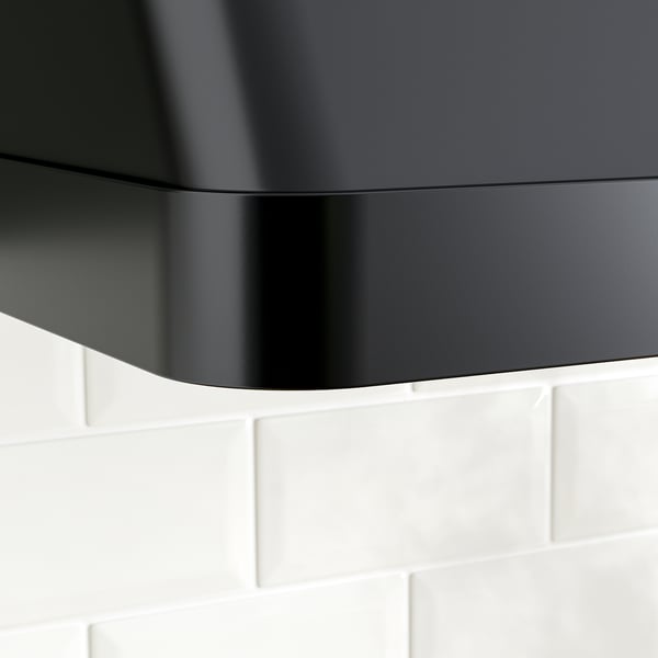 Black modern vent hood above white tiled wall, sleek curved design.