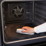 A person cleans an ovens self-cleaning feature, using a cloth. The oven has fan-forced air convection.