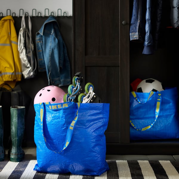 Blue IKEA FRAKTA bag containing kids helmet and roller skates beside closet with jackets and boots.