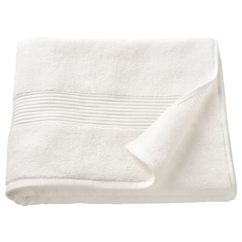 A folded white FREDRIKSJÖN towel. Its thick, soft, and made of 100% cotton. The design includes a ribbed pattern and a decorative woven border.